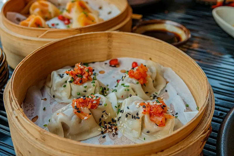 Chinese dumplings in a bamboo steamer with red chilli