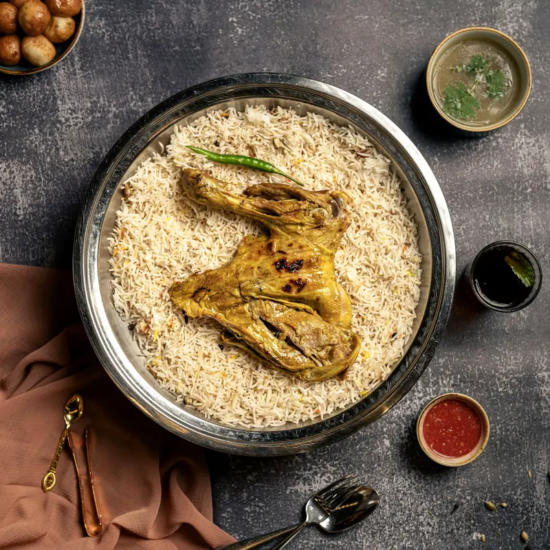 A tray of kabsa rice with lamb and side sauces